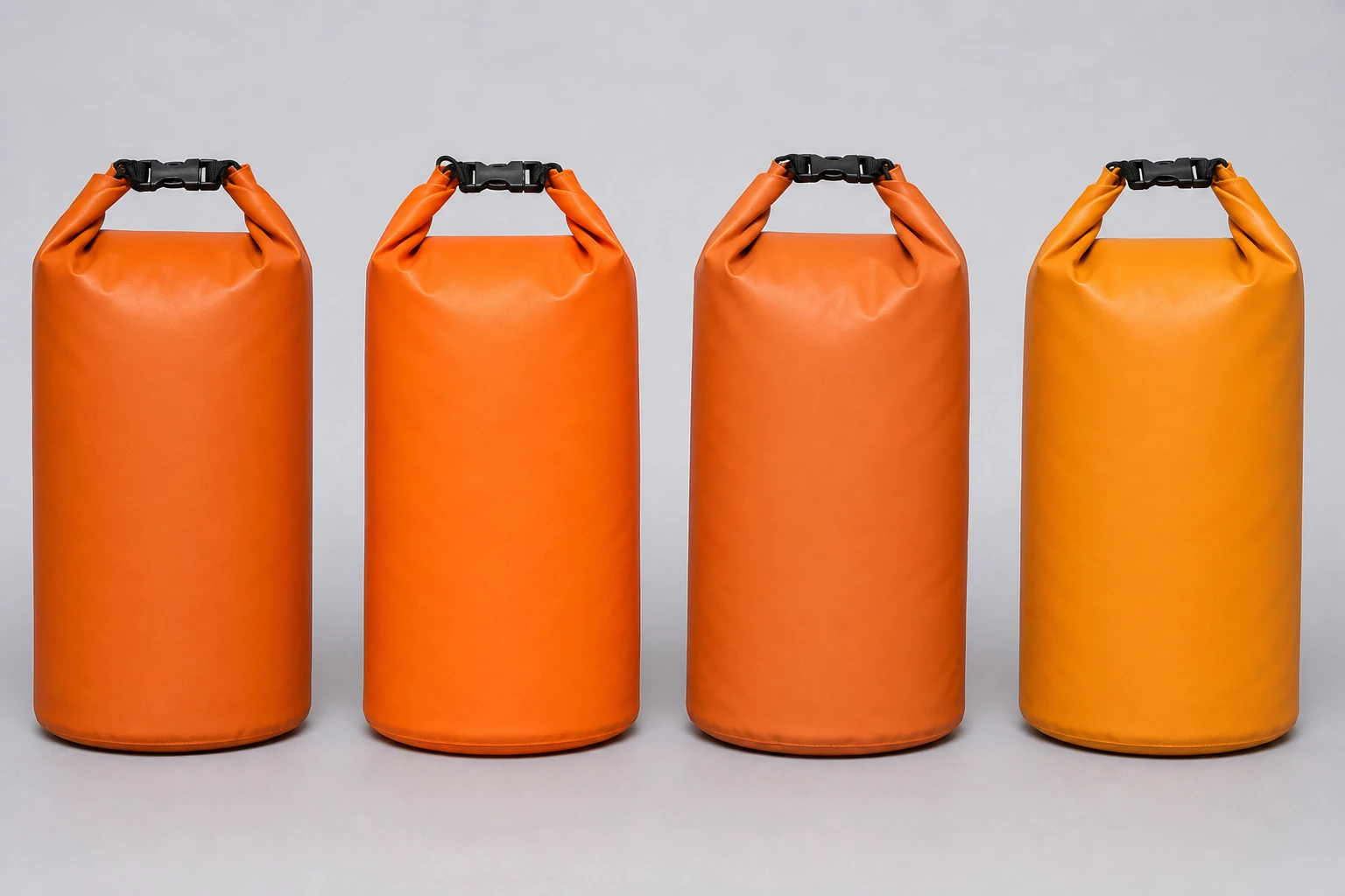 Four complete cylindrical roll-top bags in three orange shades and one yellow shade aligned under the same neutral studio light