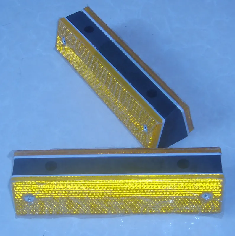 Two complete yellow roadway reflectors showing reflective faces, fasteners and side profiles