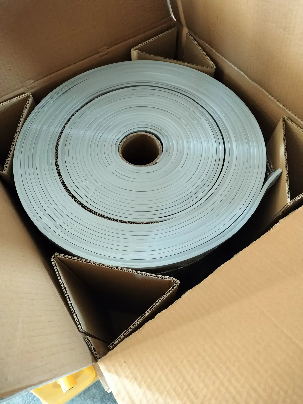 Roll of light gray flexible material protected inside a plain cardboard carton.