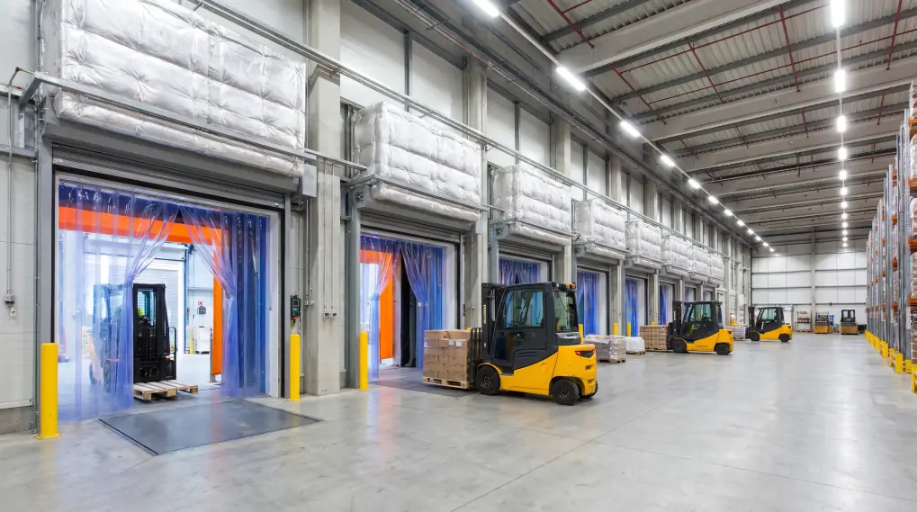 Modern warehouse loading dock with vinyl strip curtains and forklift trucks showing thermal barrier system