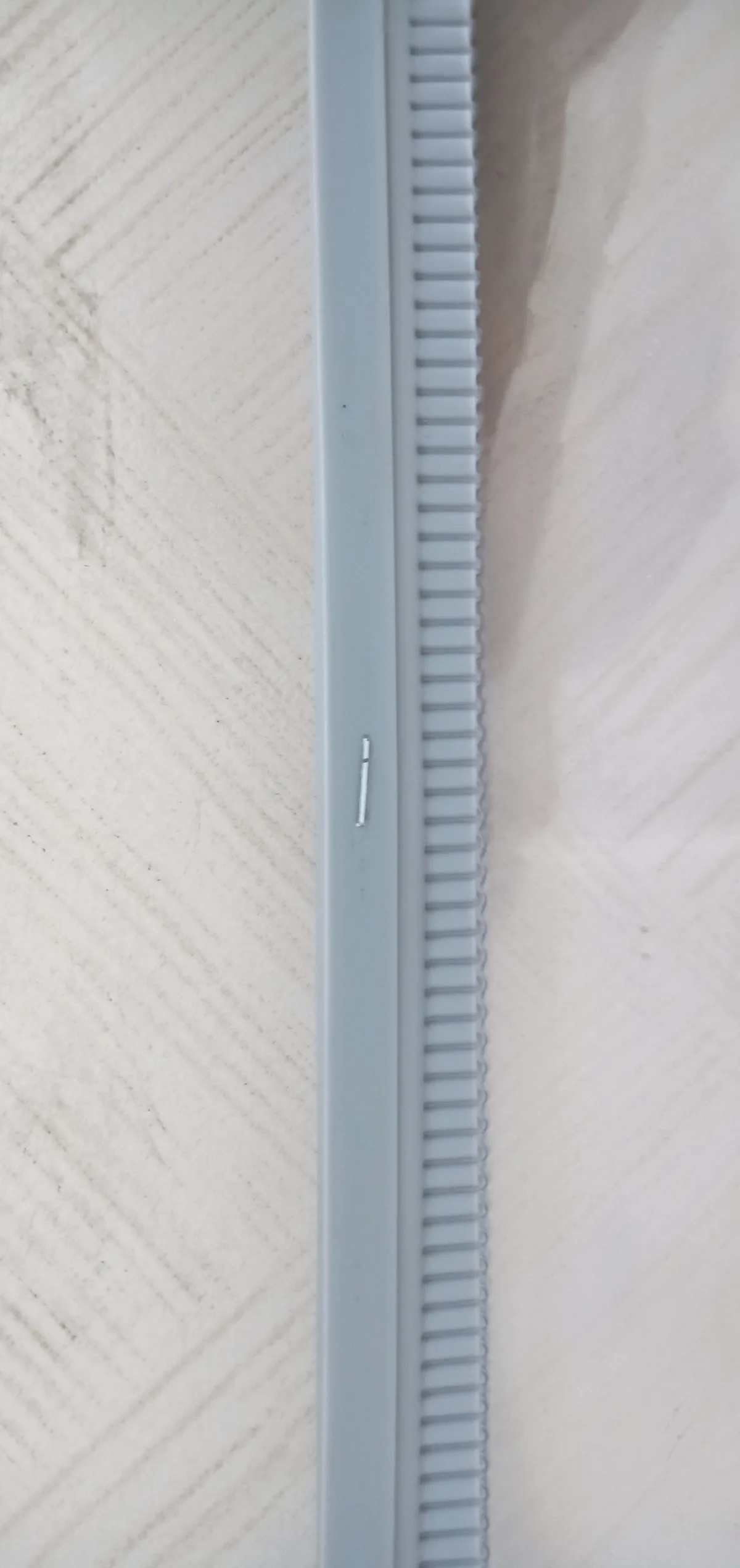 Close vertical view of a gray ribbed edge strip laid beside a clear panel surface.