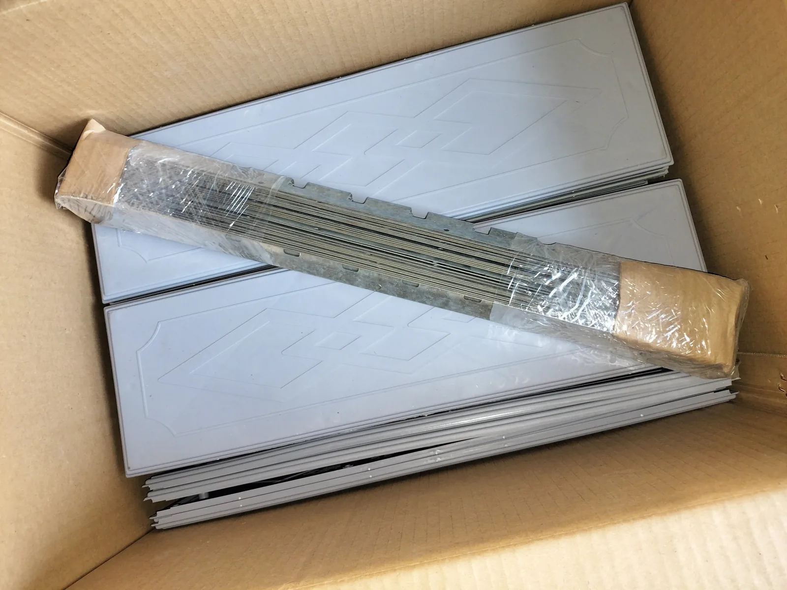 Closer view of stacked gray rectangular pieces and bundled metal strips inside a plain carton.