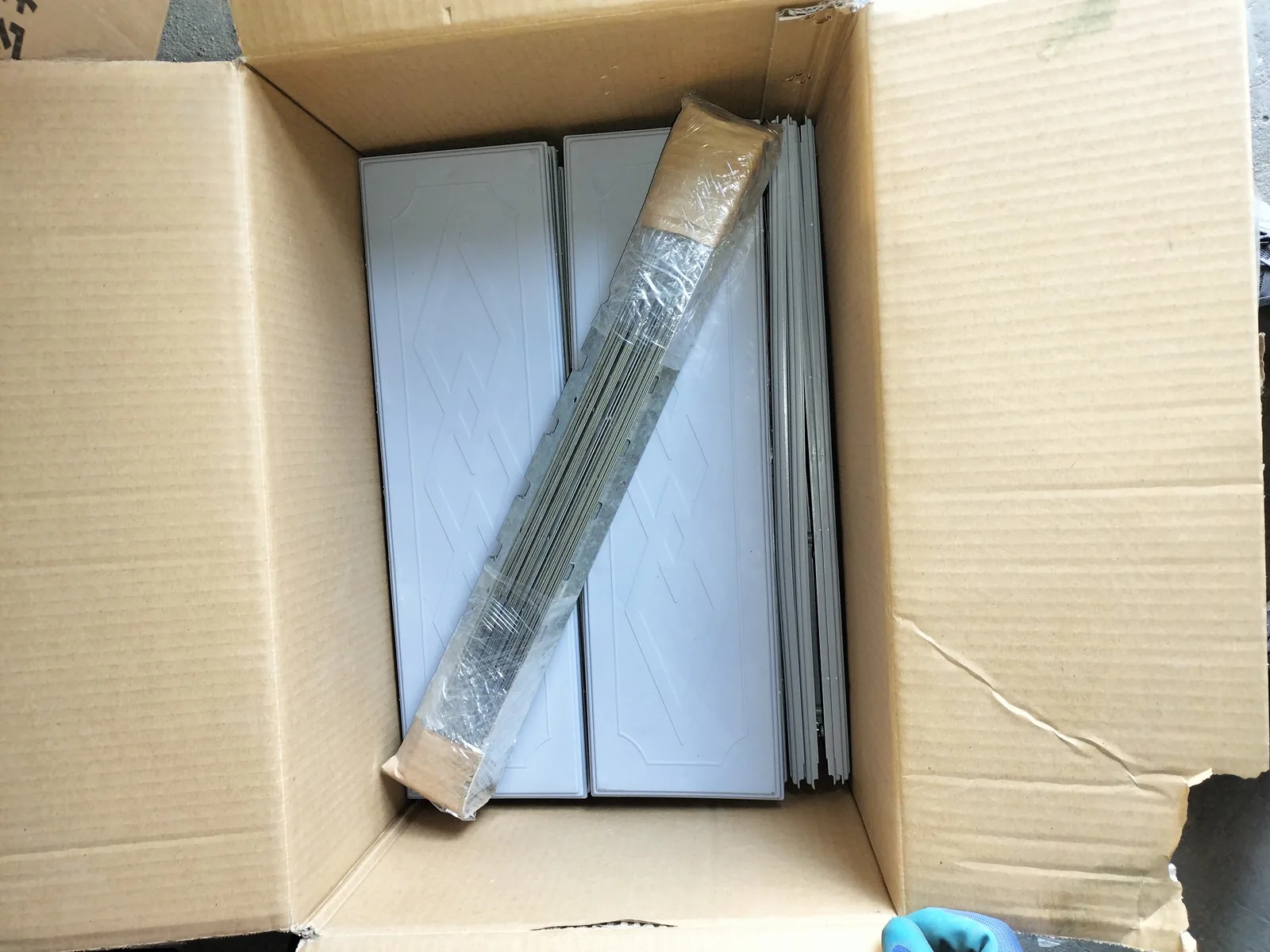 Open carton containing stacked gray rectangular pieces and a bundled set of metal strips.