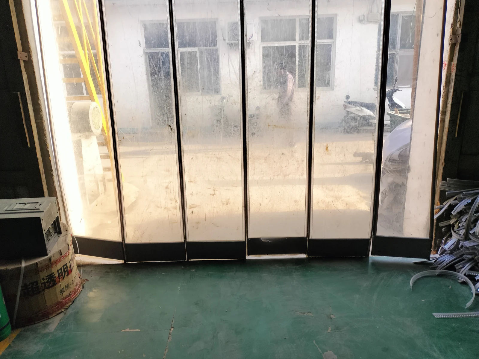 Full doorway opening fitted with transparent vertical curtain panels and dark edge strips, photographed from inside the building.