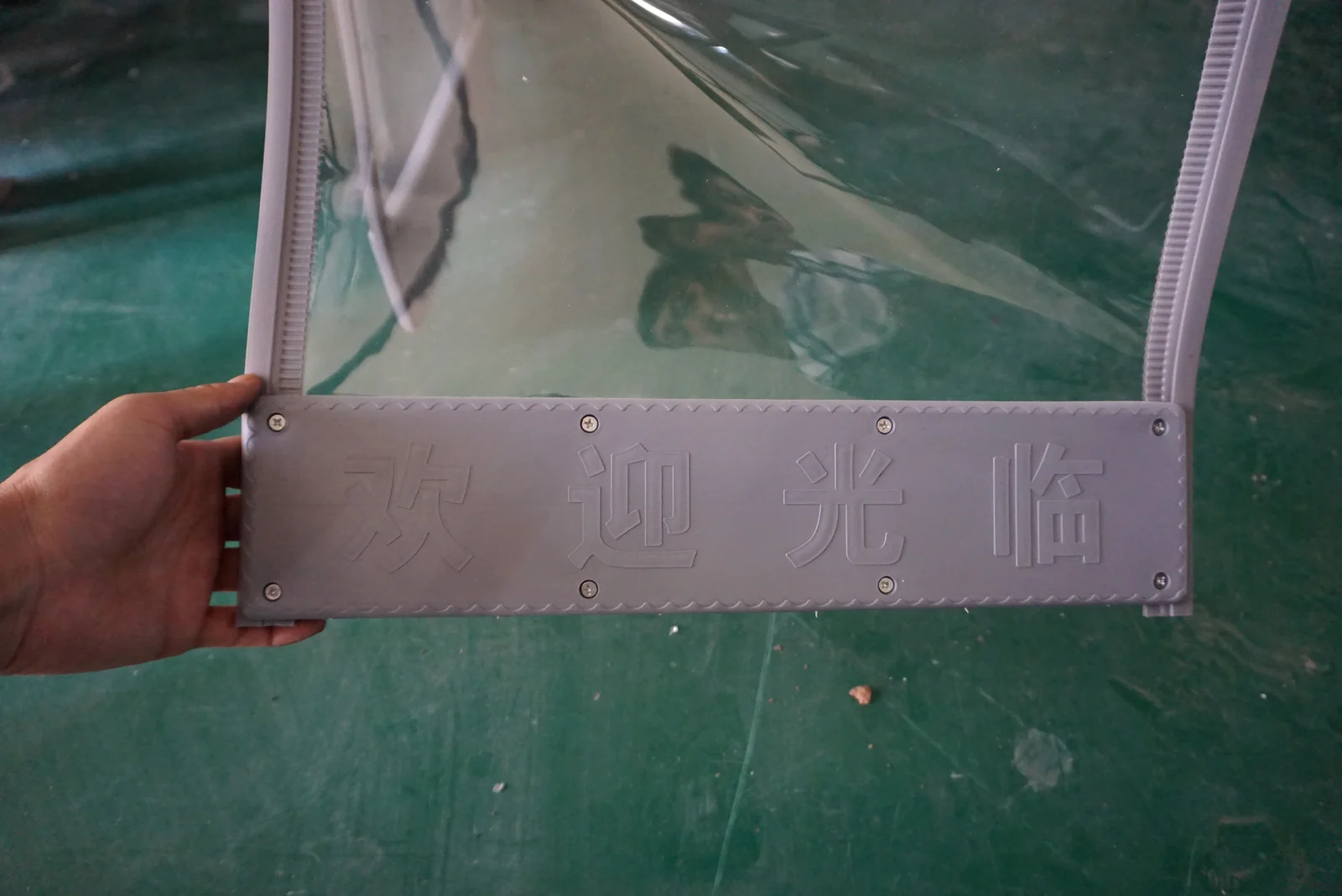 Hand holding a clear flexible panel with a gray lower section, visible fasteners and gray ribbed side edges.