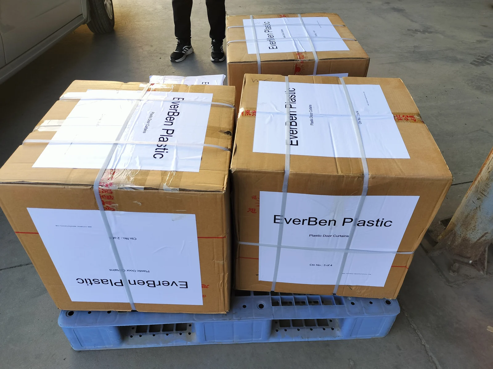 Four closed corrugated cartons strapped on a blue plastic pallet with printed EverBen Plastic door-curtain sheets attached.
